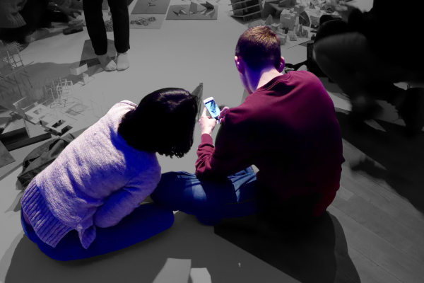 Image of 2 people looking at a phone while sitting on the floor